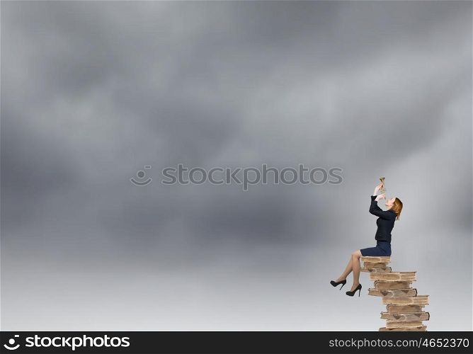 Woman speaking in horn. Young businesswoman sitting on pile of books proclaiming something in horn