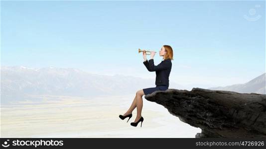 Woman speaking in horn. Young businesswoman sitting on rock edge and proclaiming something in horn