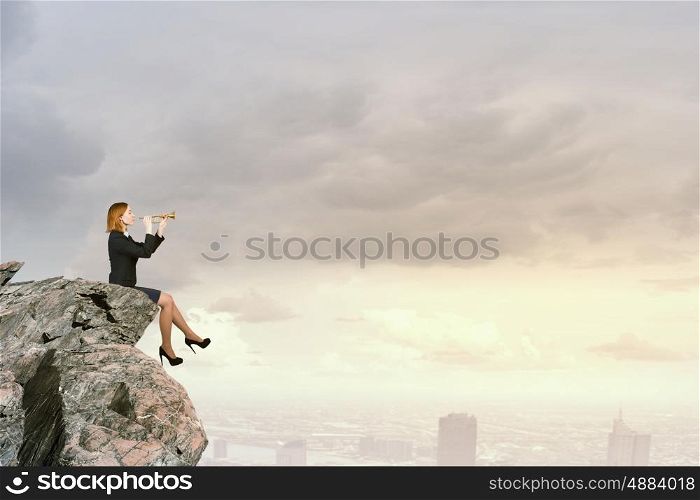 Woman speaking in horn. Young businesswoman sitting on rock edge and proclaiming something in horn