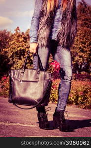 Woman spends time in park outdoor.. Rest and relax outdoor. Part body of fashionable woman wearing jeans walking in park. Girl holds black bag with pink flower resting in garden.