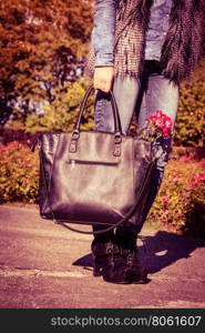 Woman spends time in park outdoor.. Rest and relax outdoor. Part body of fashionable woman wearing jeans walking in park. Girl holds black bag with pink flower resting in garden.