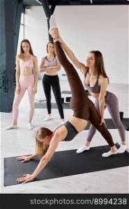 Woman sports coach helping female group with pilates exercises. Instructor stretching feet of young girl while other teammates supervising process. Woman sports coach helping female group with pilates exercises