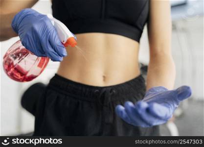 woman spraying disinfectant her gloves gym