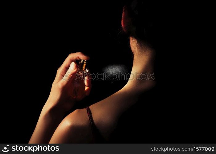 Woman sprays perfume on her neck with a black background.