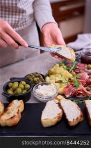 Woman spreading butter on grilled piece of baguette with Italian antipasto meat platter on background.. Woman spreading butter on grilled piece of baguette with Italian antipasto meat platter on background
