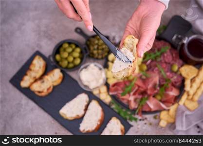 Woman spreading butter on grilled piece of baguette with Italian antipasto meat platter on background.. Woman spreading butter on grilled piece of baguette with Italian antipasto meat platter on background