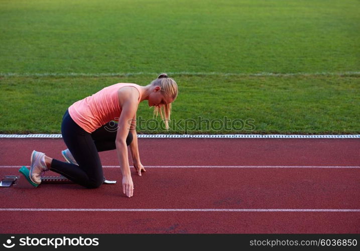 woman sprinter leaving starting blocks on the athletic track. Side view. exploding start