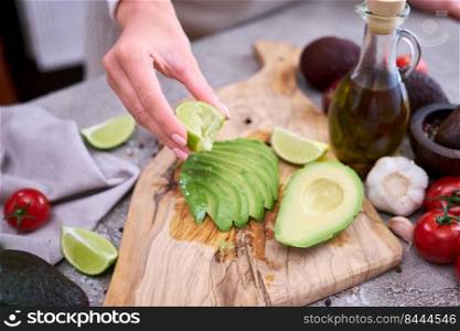 woman squeeze fresh lime juice onto Sliced avocado on wooden cutting board at domestic kitchen.. woman squeeze fresh lime juice onto Sliced avocado on wooden cutting board at domestic kitchen
