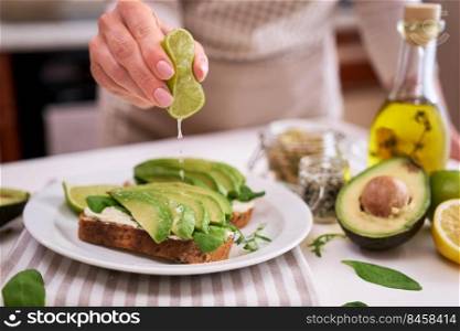 Woman squeezing fresh lime juice on a Avocado and cream cheese toasts.. Woman squeezing fresh lime juice on a Avocado and cream cheese toasts