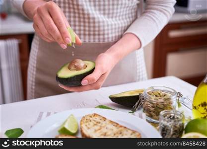 Woman squeezing fresh lime juice on a halved avocado at domestic kitchen.. Woman squeezing fresh lime juice on a halved avocado at domestic kitchen