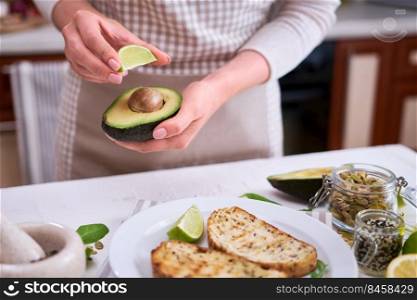 Woman squeezing fresh lime juice on a halved avocado at domestic kitchen.. Woman squeezing fresh lime juice on a halved avocado at domestic kitchen