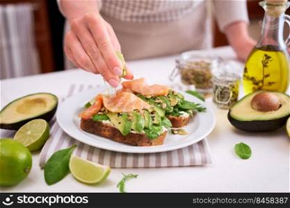 Woman squeezing lime juice on Freshly made Avocado, salmon and cream cheese toasts.. Woman squeezing lime juice on Freshly made Avocado, salmon and cream cheese toasts