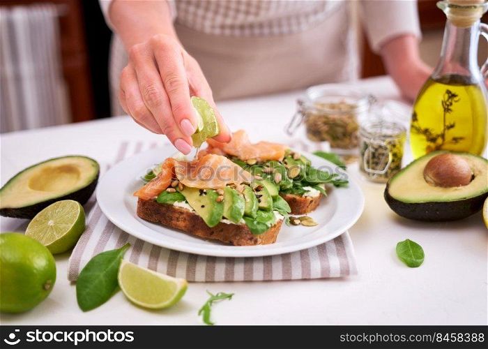 Woman squeezing lime juice on Freshly made Avocado, salmon and cream cheese toasts.. Woman squeezing lime juice on Freshly made Avocado, salmon and cream cheese toasts