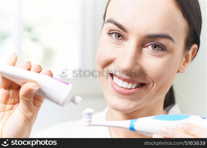 Woman Squeezing Toothpaste Onto Electric Toothbrush In Bathroom
