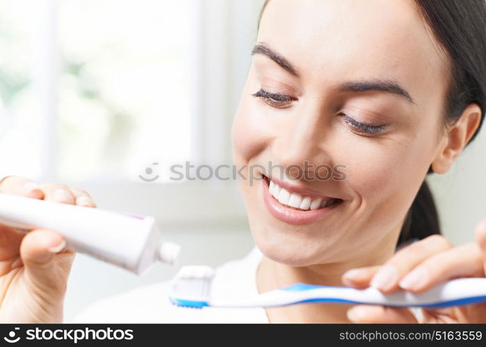 Woman Squeezing Toothpaste Onto Tootbrush In Bathroom