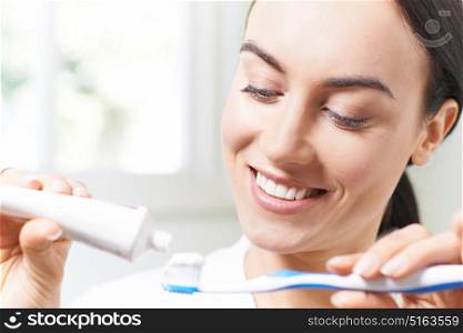 Woman Squeezing Toothpaste Onto Tootbrush In Bathroom