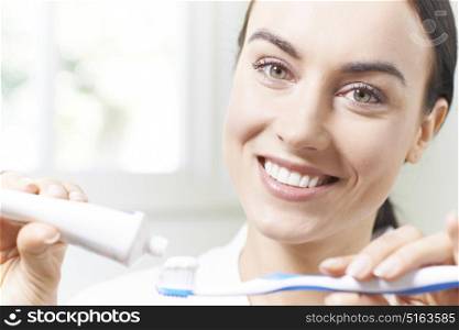Woman Squeezing Toothpaste Onto Tootbrush In Bathroom