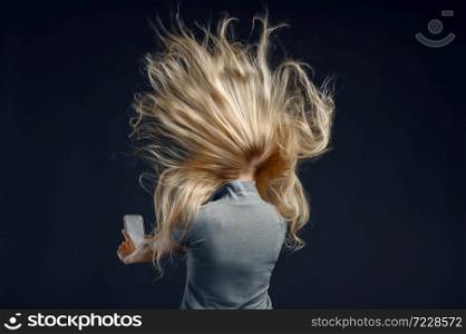 Woman standing against powerful airflow in studio, back view, developing hairstyle effect. Female person and wind, lady isolated on dark background. Woman standing against powerful airflow, back view