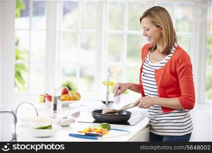 Woman Standing At Hob Preparing Meal In Kitchen