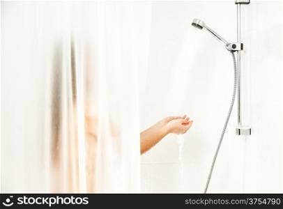 Woman standing behind curtain at shower and holding hands under water