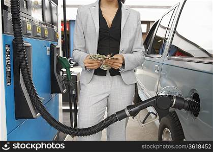 Woman standing by van with fuel pump counting money, mid section