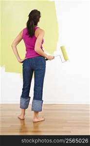 Woman standing holding paint roller admiring partially painted interior wall.
