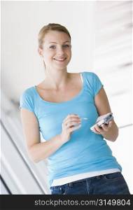 Woman standing in corridor using personal digital assistant smiling