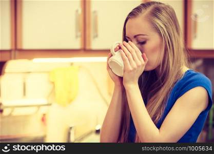 Woman standing in kitchen holding cup of tea of coffee enjoying her relaxing free time.. Woman holding cup of tea of coffee