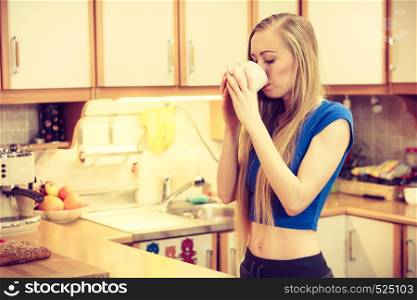 Woman standing in kitchen holding cup of tea of coffee enjoying her relaxing free time.. Woman holding cup of tea of coffee