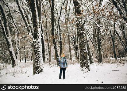 Woman standing in snow-covered forest looking away