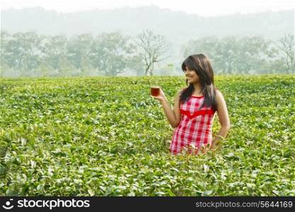 Woman standing in tea plantation with a cup of tea