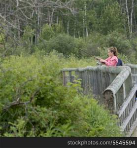 Woman standing on a footbridge and fishing, Riding Mountain National Park, Manitoba, Canada