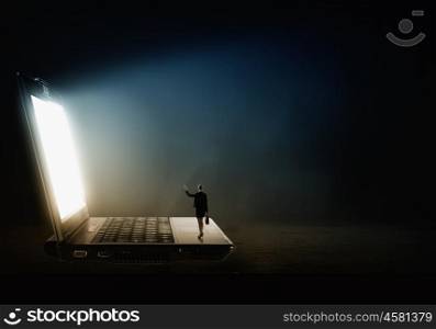 Woman standing on big laptop. Rear view of businesswoman with suitcase standing on keyboard of big laptop