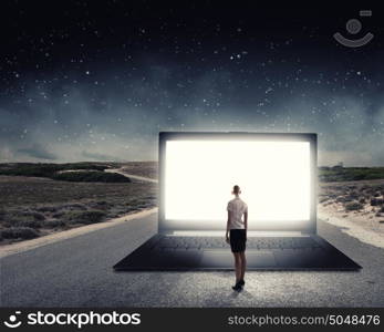 Woman standing on big laptop. Rear view of businesswoman with suitcase standing on keyboard of big laptop