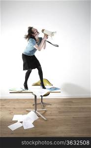Woman standing on desk, shouting through megaphone