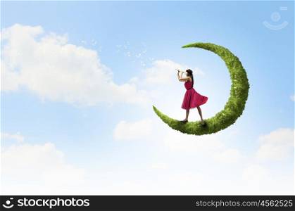 Woman standing on green moon. Young woman in red dress playing flute