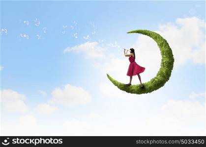 Woman standing on green moon. Young woman in red dress playing flute
