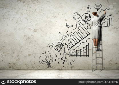 Woman standing on ladder drawing on wall. Image of businesswoman standing on ladder and drawing on wall