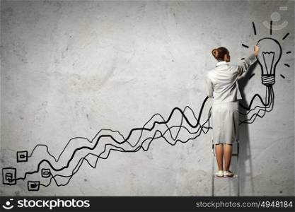 Woman standing on ladder drawing on wall. Image of businesswoman standing on ladder and drawing on wall