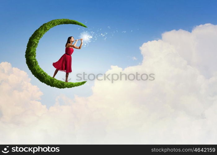 Woman standing on moon. Young woman in red dress playing flute