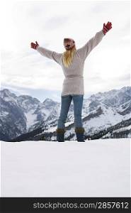 Woman standing on mountain peak with arms outstretched back view