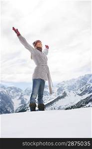 Woman standing on mountain peak with arms outstretched side view