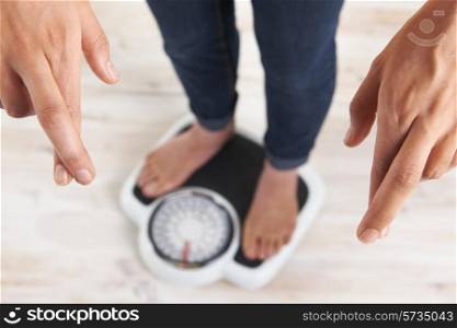 Woman Standing On Scales With Fingers Crossed