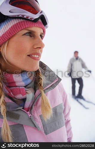 Woman standing on ski slope man on skis in background