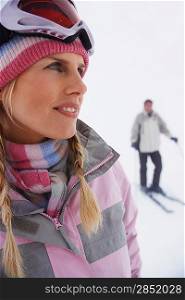 Woman standing on ski slope man on skis in background