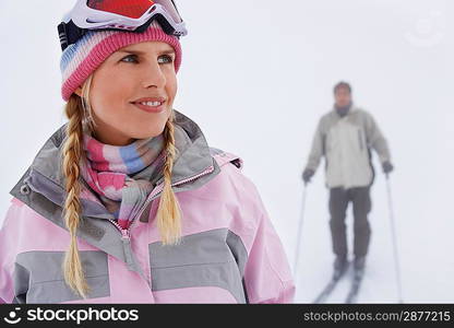 Woman standing on ski slope man on skis in background