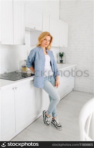 Woman standing on the kitchen with snow-white interior. Female person at home in the morning, healthy nutrition and lifestyle
