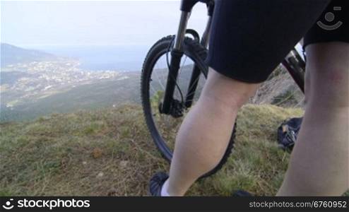 Woman standing on top of mountain with bicycle and enjoying view