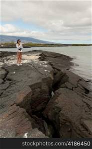 Woman standing on volcanic rock on the coast, Punta Espinoza, Fernandina Island, Galapagos Islands, Ecuador