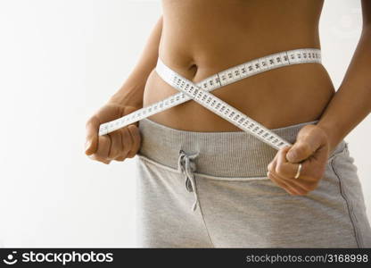 Woman standing pulling measuring tape around waist.